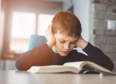 Child reading a book at the desk. 8 years old boy tired doing his homework at the table